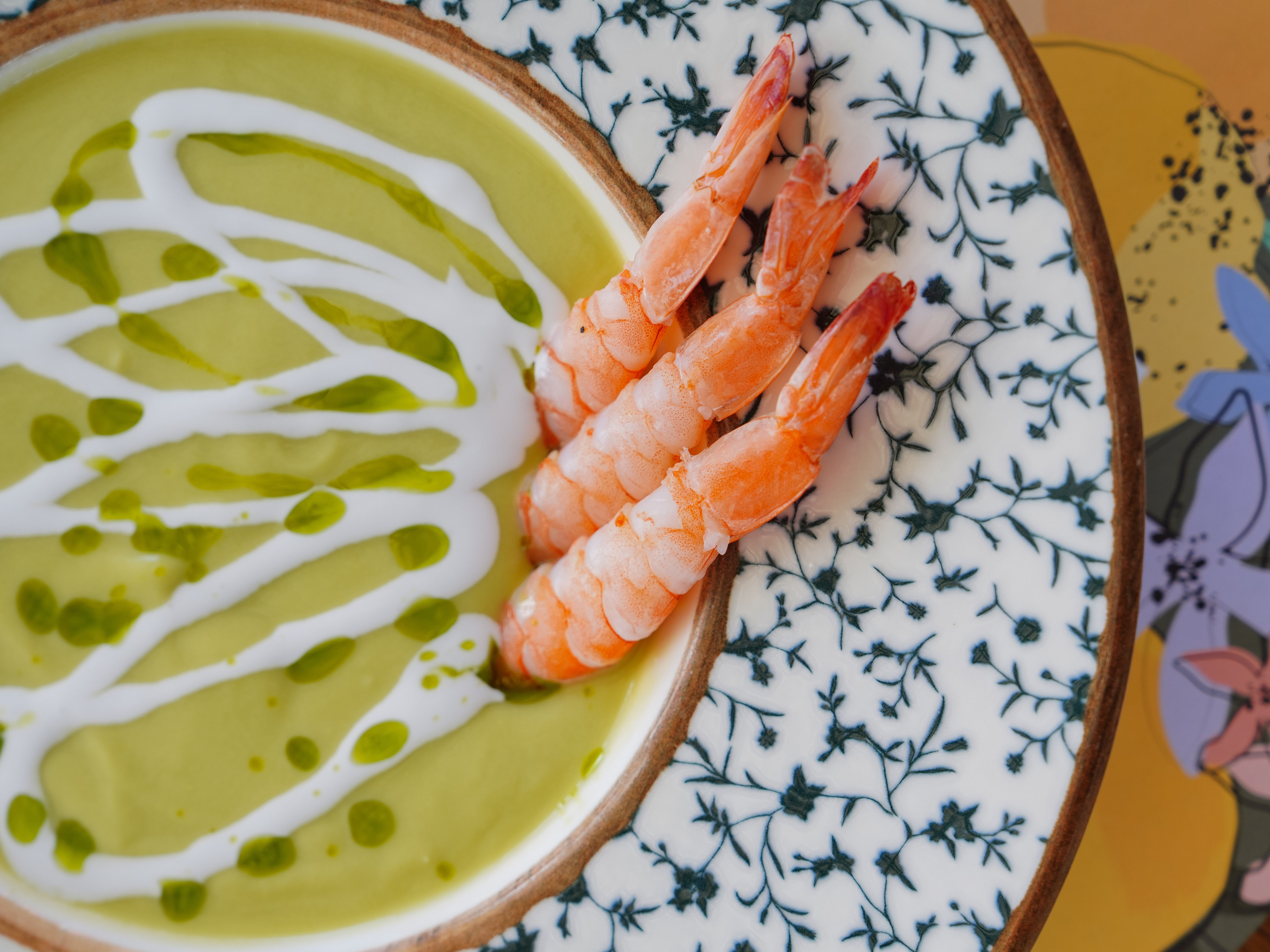 Kalte Avocado Tomaten Suppe A close-up shot of shrimp served on avocado soup in a decorative bowl, garnished with cream and herbs.