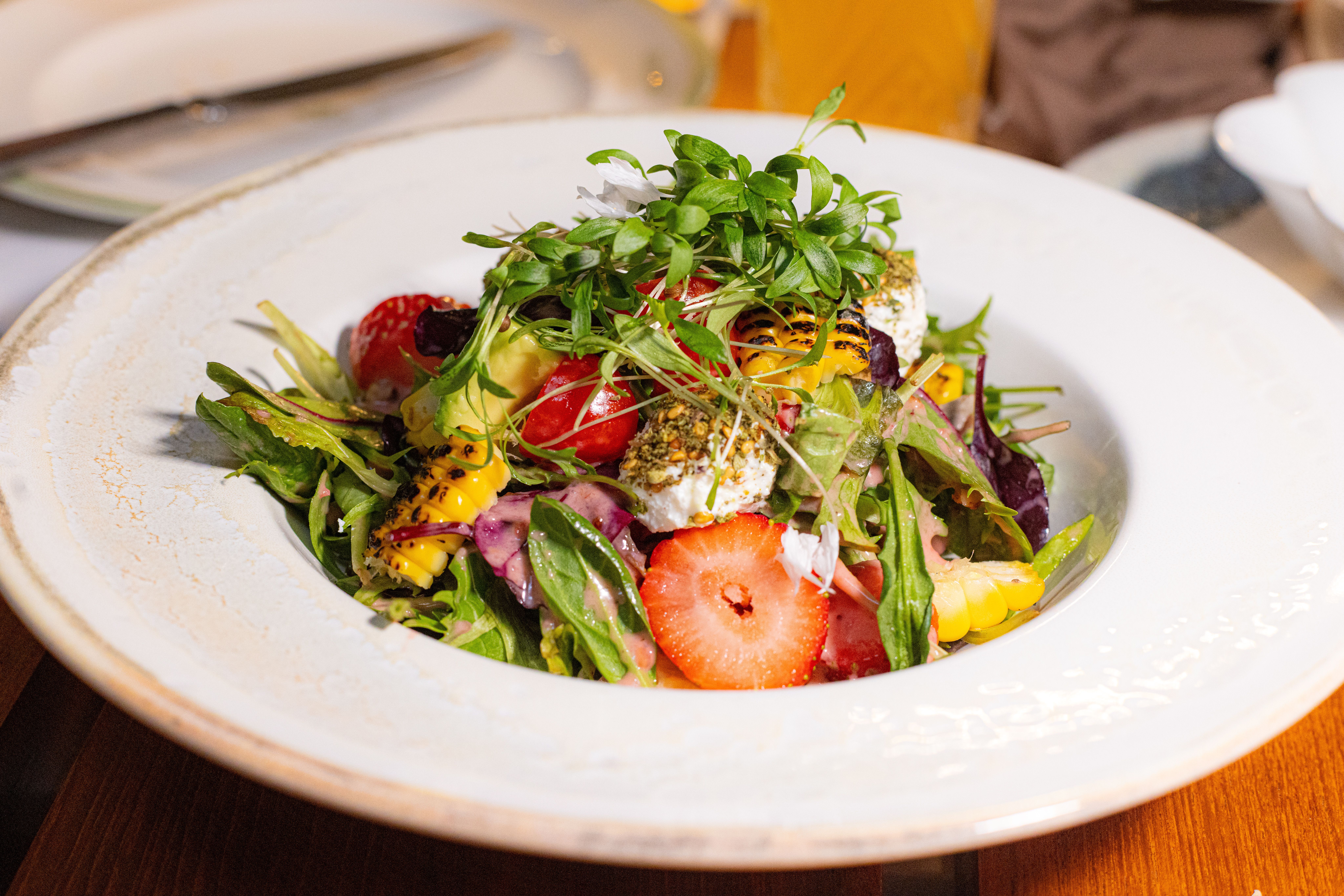 Spargelsalat mit Erdbeeren und Rhabarber Colorful summer salad with strawberries, greens, and cheese in a white bowl.
