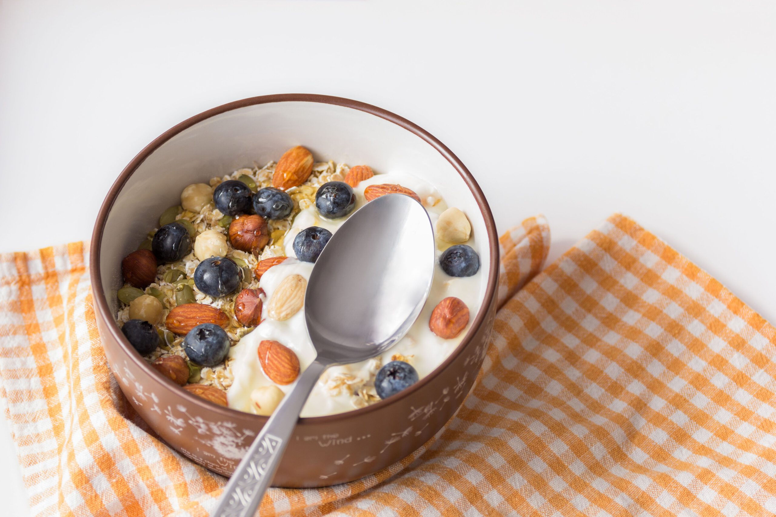 Studi Joghurt A delicious breakfast bowl featuring yogurt, nuts, and fresh blueberries on a checkered cloth.