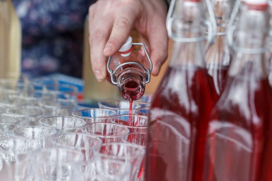 Hand pouring vibrant red liquid into multiple shot glasses, perfect for party or celebration themes.